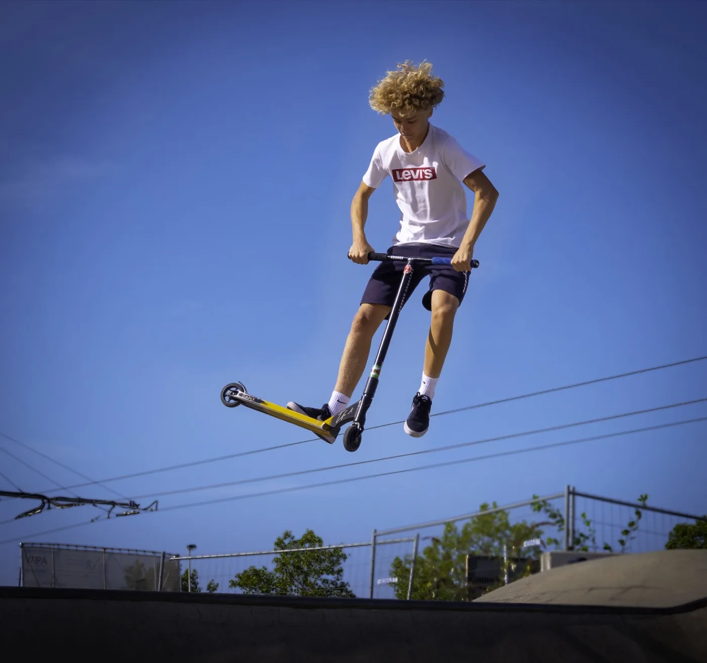 Tiener in de lucht op een stuntstep boven een skatepark